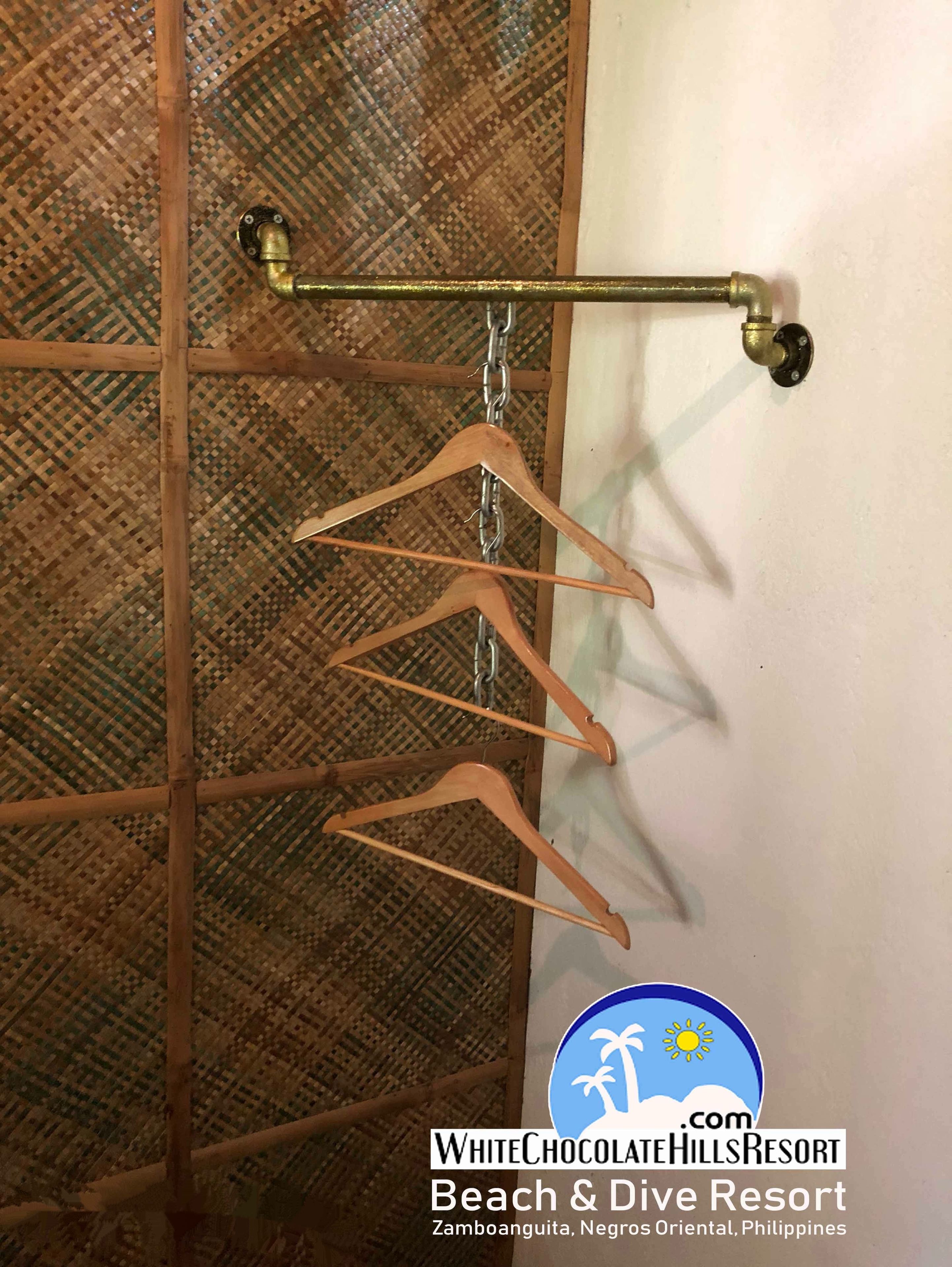 A wooden hanger rack with multiple hangers against a wall with a woven pattern.