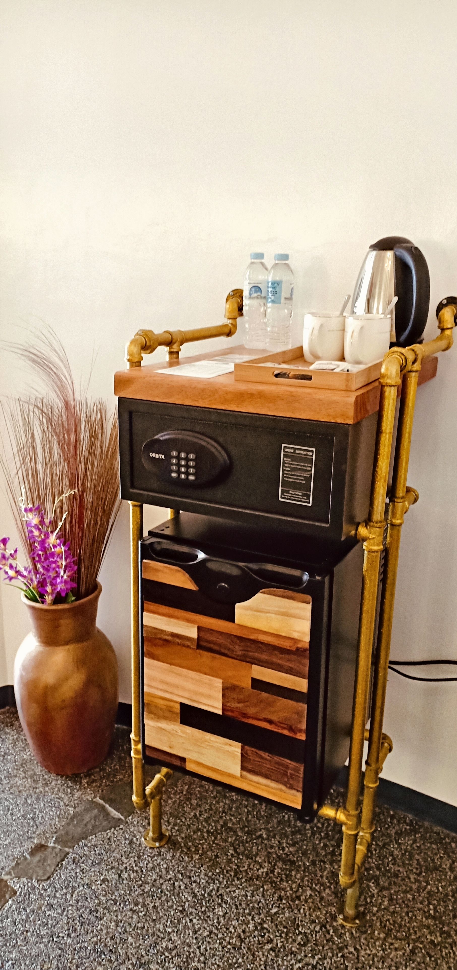 A minibar with a wooden top, brass pipes, and a black control panel.