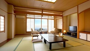 A traditional Japanese room with tatami flooring, a low table, chairs, a television, and a view through large windows. - Tsukagoshiya (Shibukawa-shi)