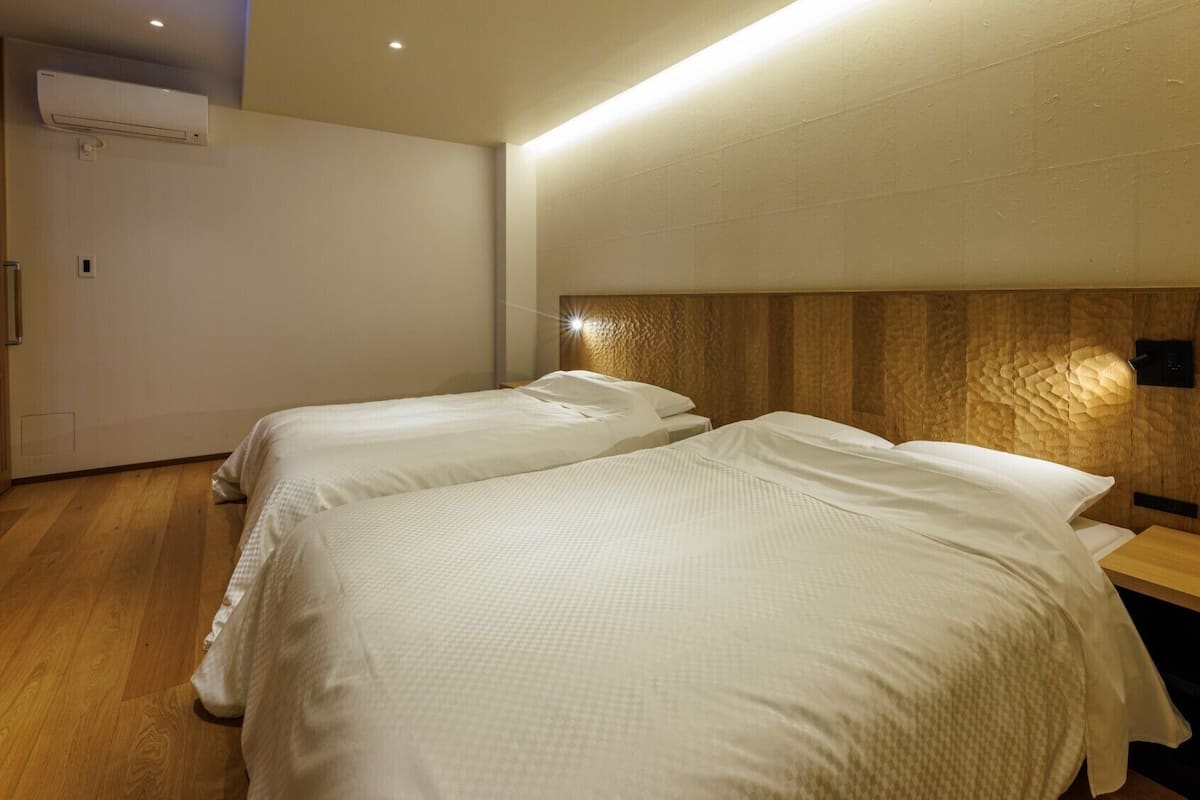 A hotel room with two beds, a wooden headboard, a bedside table, and an air conditioning unit.