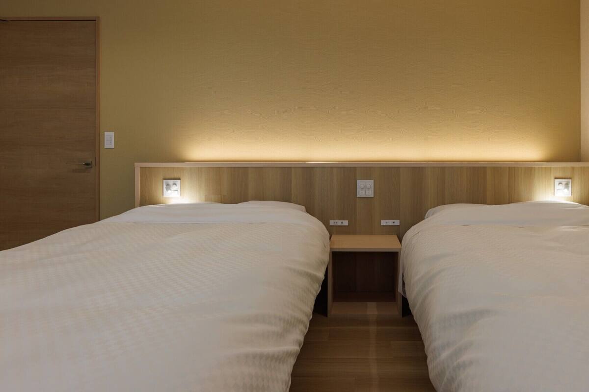 A hotel room with two beds, wooden headboards, bedside tables, and wall-mounted light fixtures.