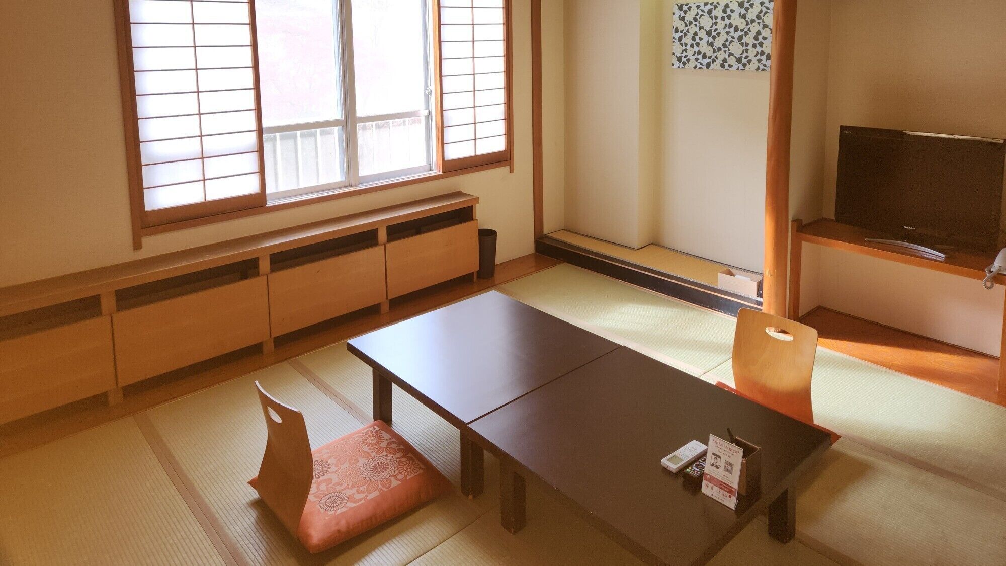 A traditional Japanese room with tatami flooring, a low table, a cushion, a television, and a sliding door.