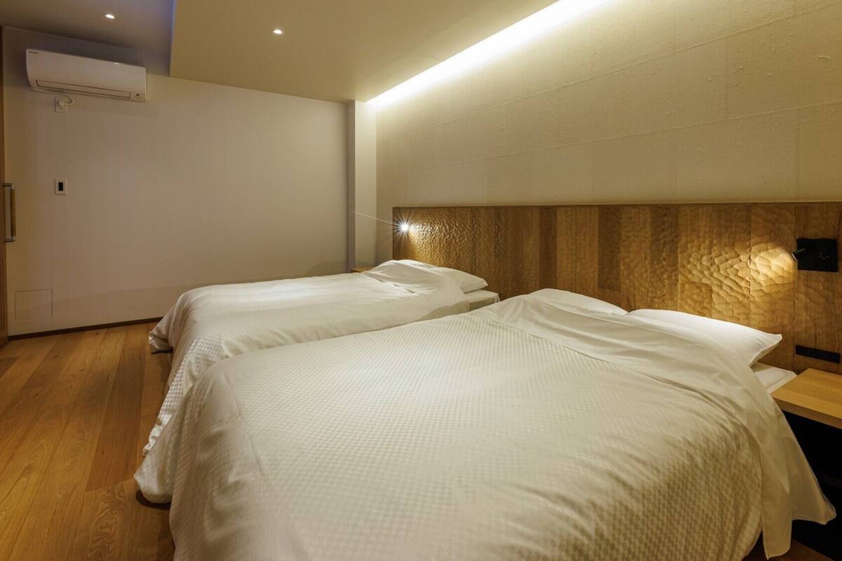 A hotel room with two beds, a wooden headboard, a bedside table, and an air conditioning unit.