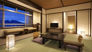 A traditional Japanese room with tatami flooring, a low table, seating, a television, and a view of mountains. - Tsukagoshiya (Shibukawa-shi)