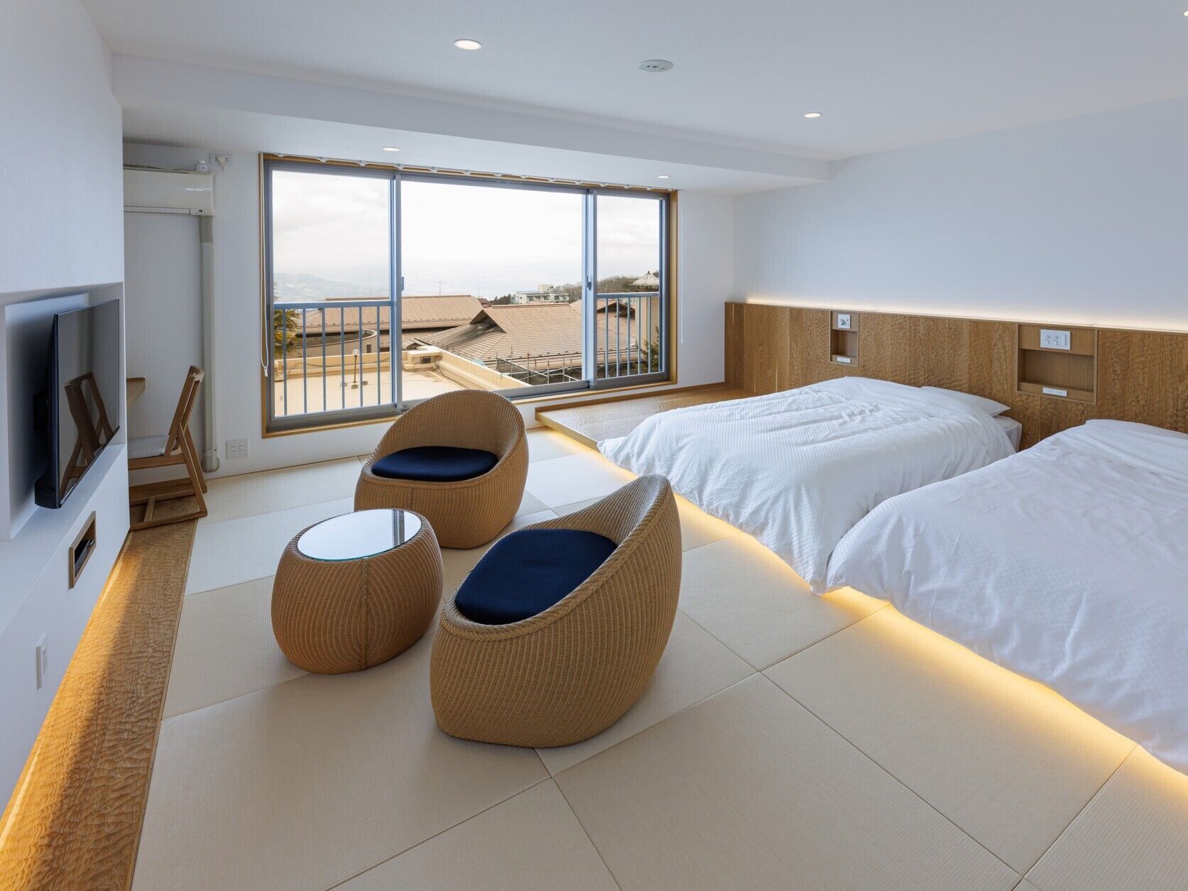 A modern hotel room with two beds, a TV, and a balcony with a view.