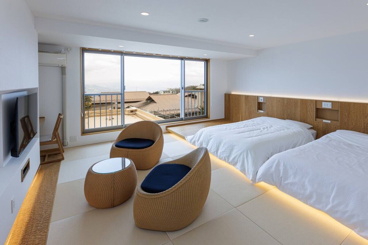 A modern hotel room with two beds, a TV, and a balcony with a view.