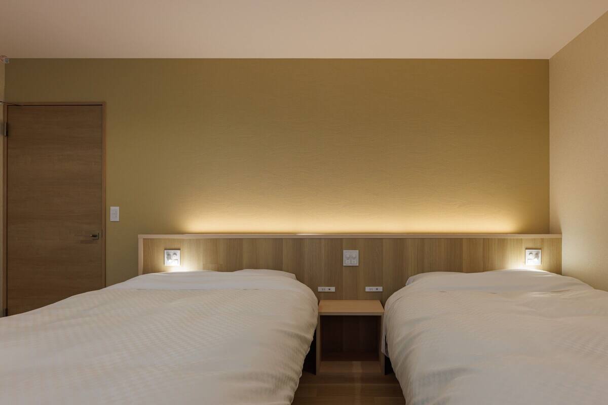 A hotel room with two beds, wooden headboard, bedside tables, and wall-mounted lights.