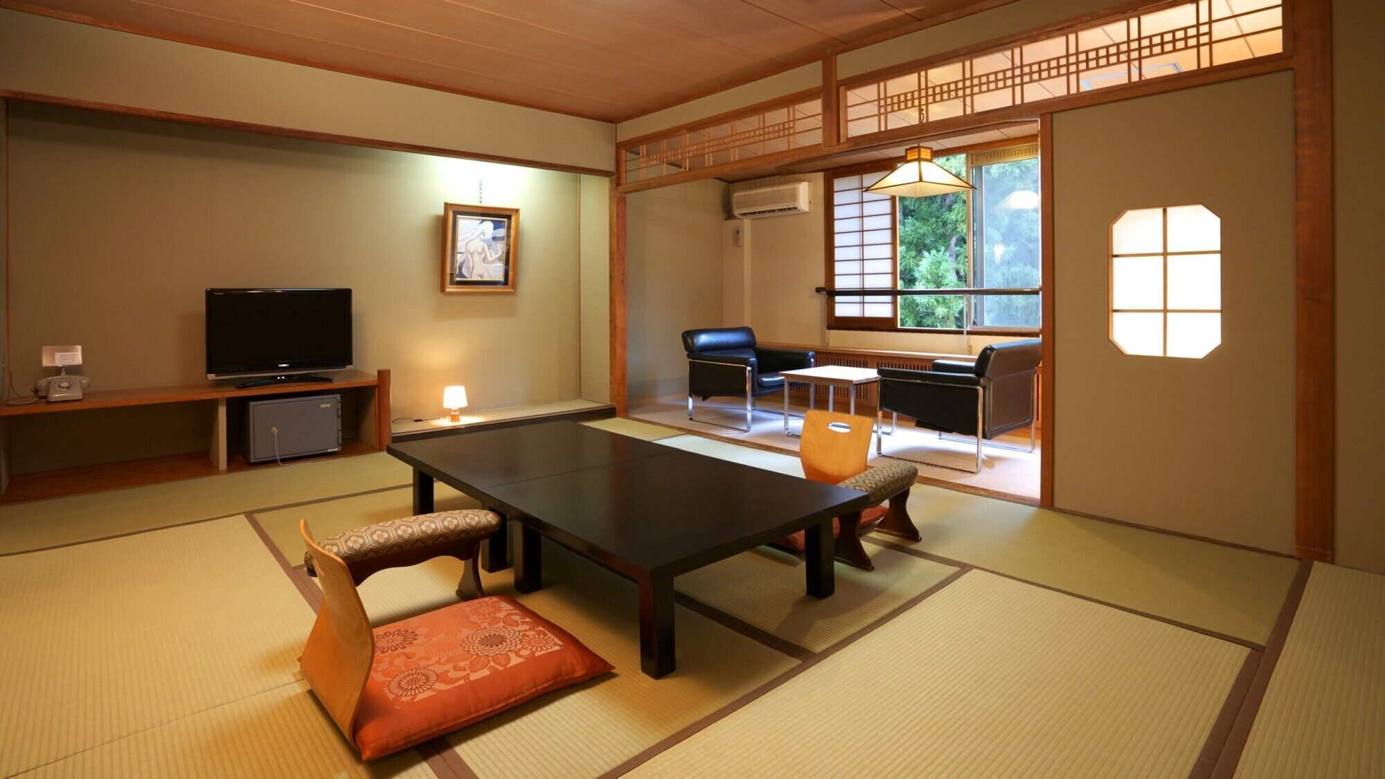 A traditional Japanese room with tatami flooring, a low table with cushions, a television, and a sliding door leading to a seating area with a view of greenery.
