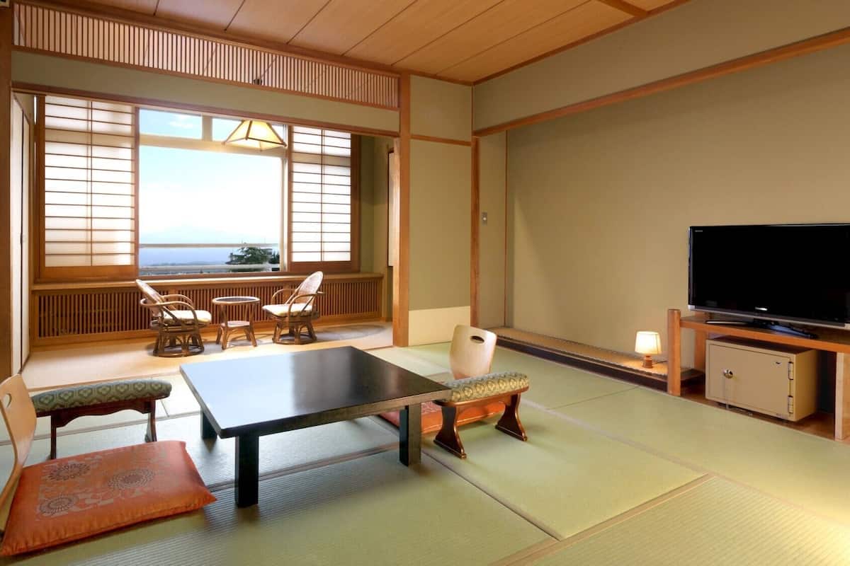 Une pièce de style japonais traditionnel, avec un sol recouvert de tatamis, une table basse, des chaises, un téléviseur et une vue sur l’océan.