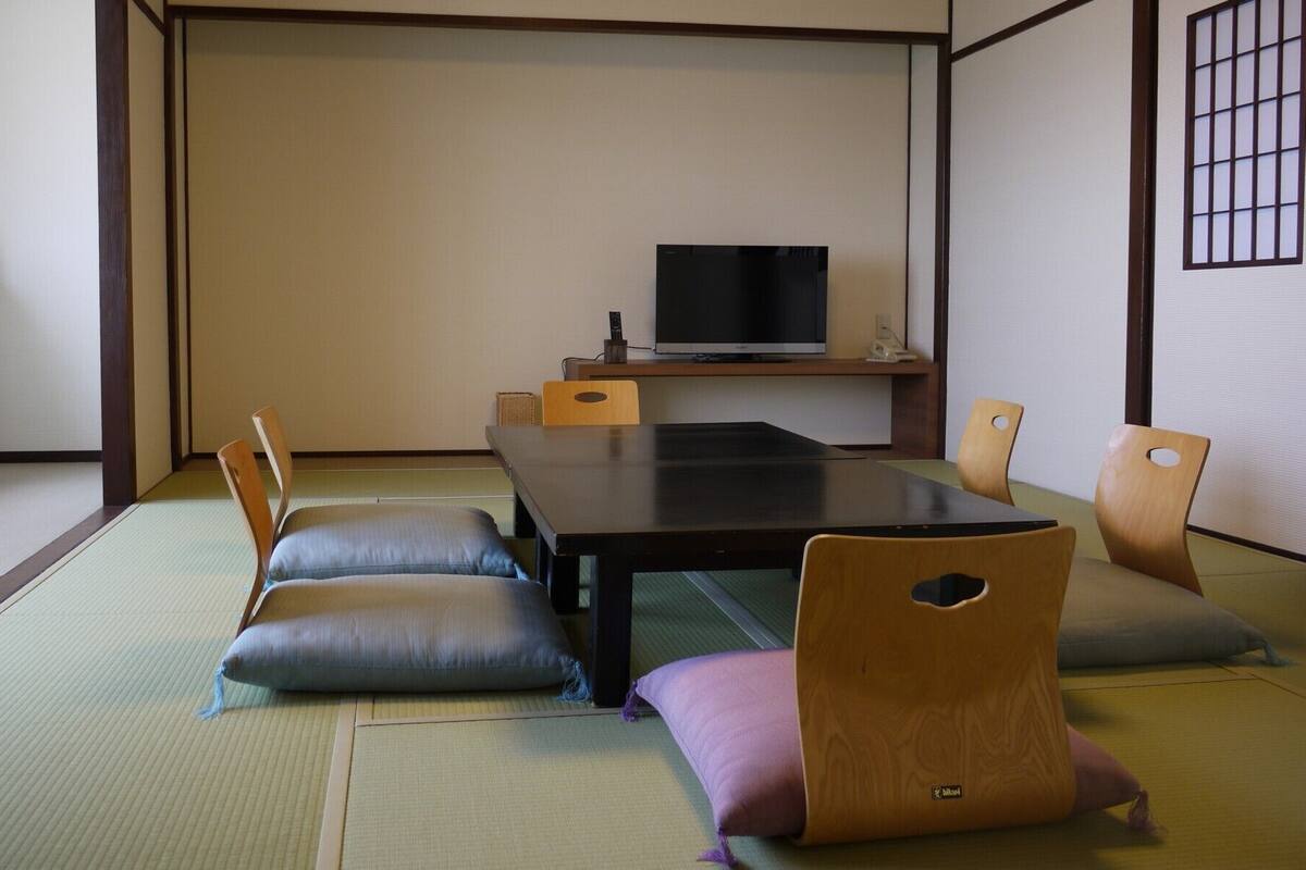 A tatami mat room with a low table, cushions, a television, and a small shelf.