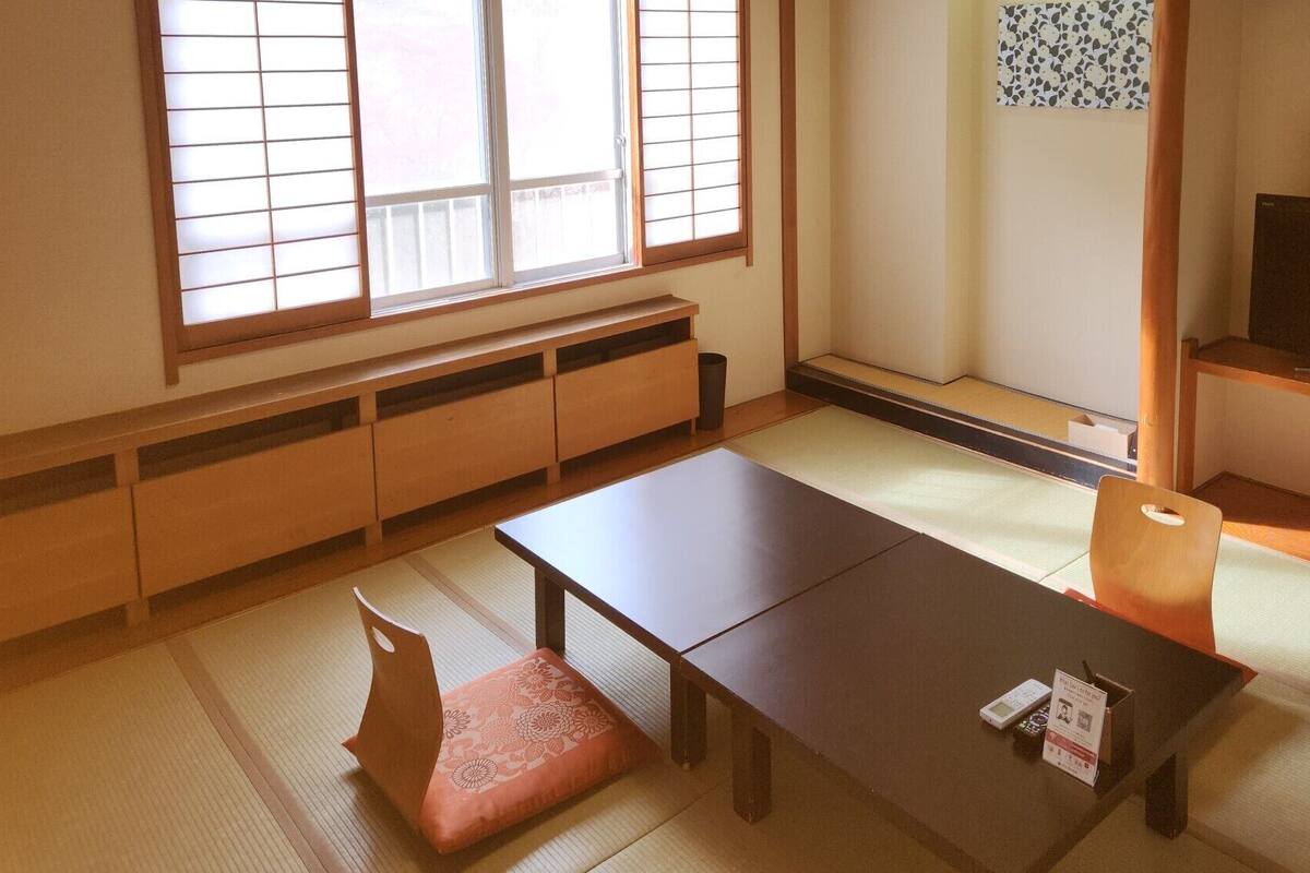 A traditional Japanese room with tatami flooring, a low table, a cushion, a television, and a sliding door.