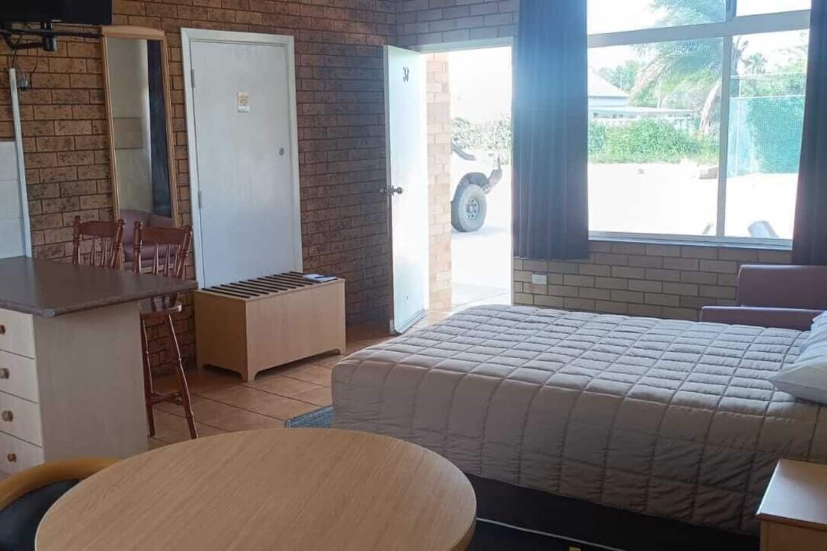 A compact room with a bed, a small kitchenette, a dining table, and a window with a view of the outside.