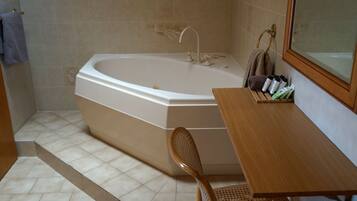 A bathroom with a large bathtub, a wooden vanity, a chair, and a shelf with toiletries.