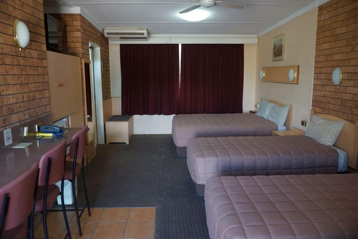 A hotel room with two beds, a desk with chairs, an air conditioning unit, and a window with curtains.