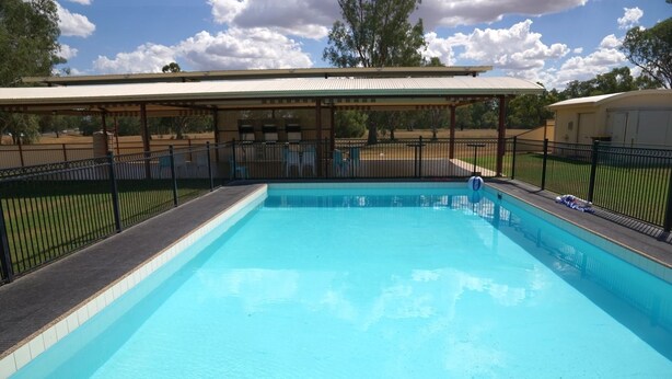 A rectangular swimming pool with a covered seating area and a fenced deck. - Nandewar Motor Inn (Narrabri)