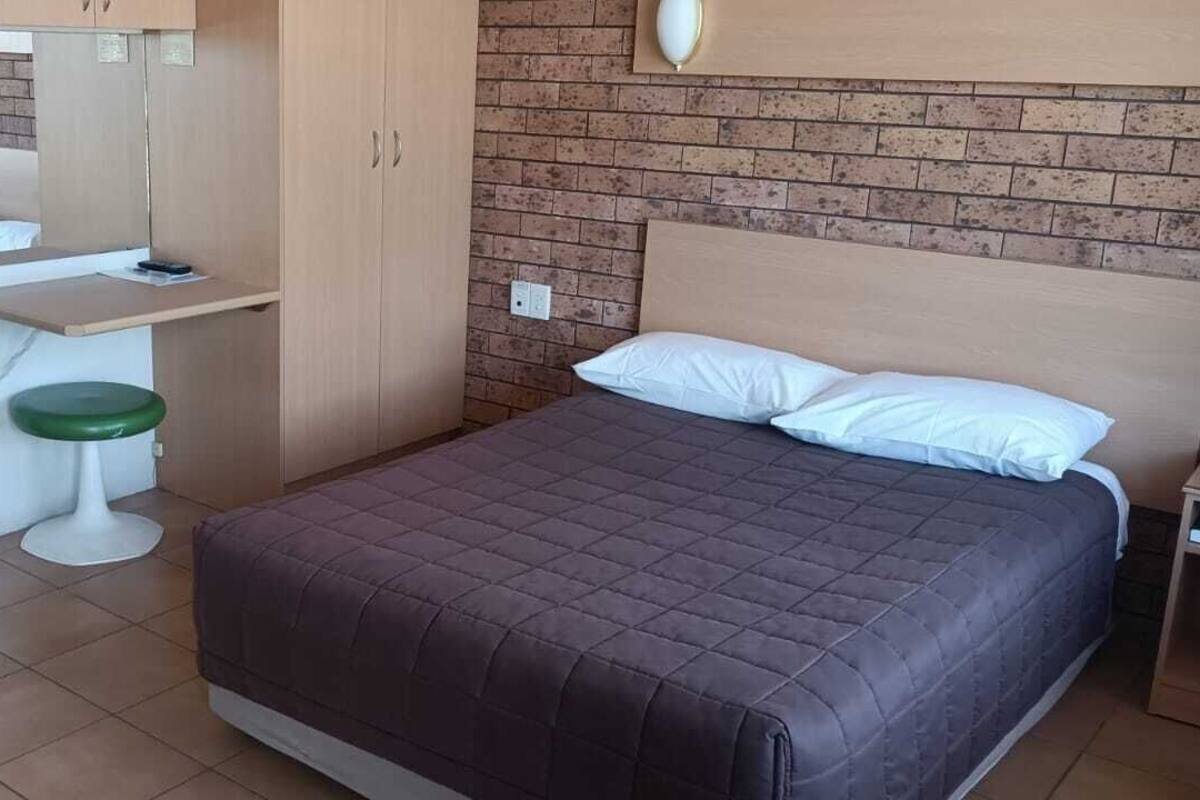 A bedroom with a bed, a small desk, a chair, a sink, and a toilet.