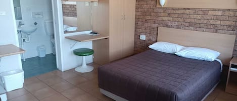 Un dormitorio con cama, escritorio pequeño, silla, lavabo y retrete.