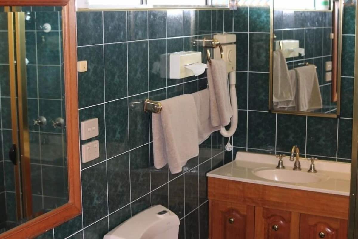 A bathroom with dark green tiles, a wooden cabinet, a sink with a mirror, and a towel rack.