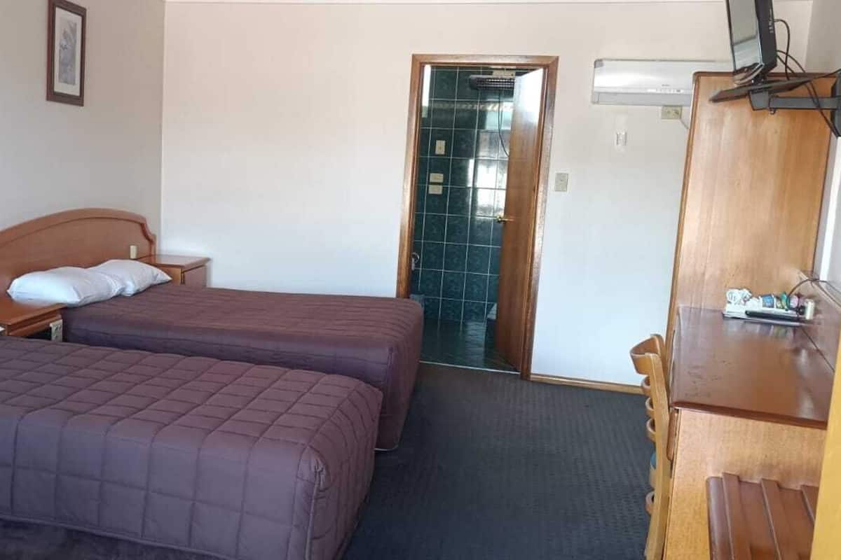 A room with two beds, a wooden wardrobe, a small table, and a door leading to a bathroom.