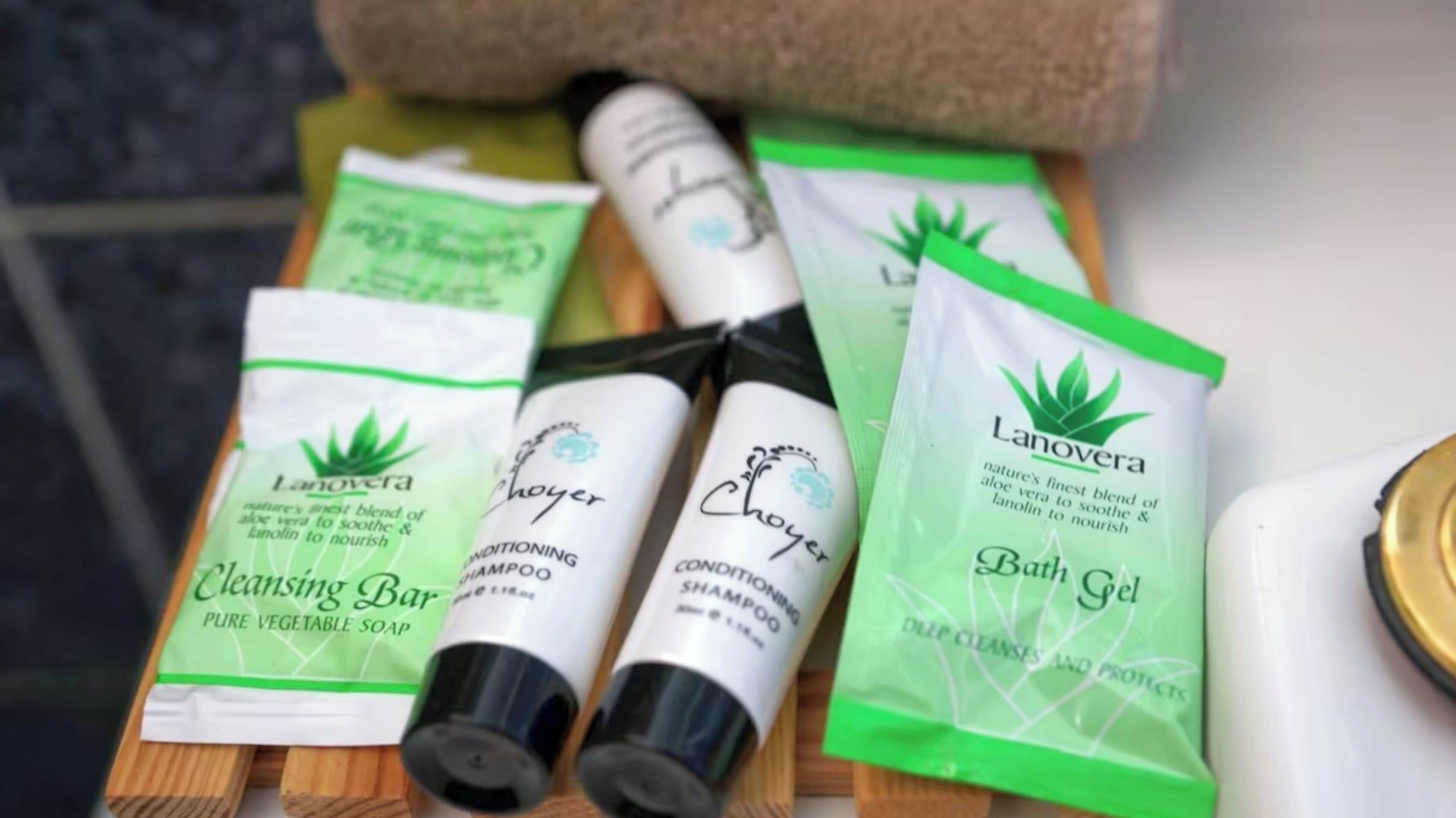 A wooden surface with various Lanovera skincare products including a cleansing bar, shampoo, conditioner, and bath gel.
