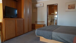 A bedroom with a bed, a television on a wooden cabinet, a wardrobe, and a bathroom visible through an open door. - Nandewar Motor Inn (Narrabri)
