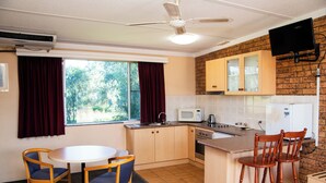 A compact kitchen with a dining area, a ceiling fan, a microwave, and a TV mounted on the wall. - Nandewar Motor Inn (Narrabri)