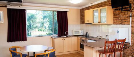 A compact kitchen with a dining area, a ceiling fan, a microwave, and a TV mounted on the wall.