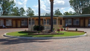 A building with a brick facade, a covered outdoor seating area, and a landscaped garden with a circular brick pathway. - Nandewar Motor Inn (Narrabri)