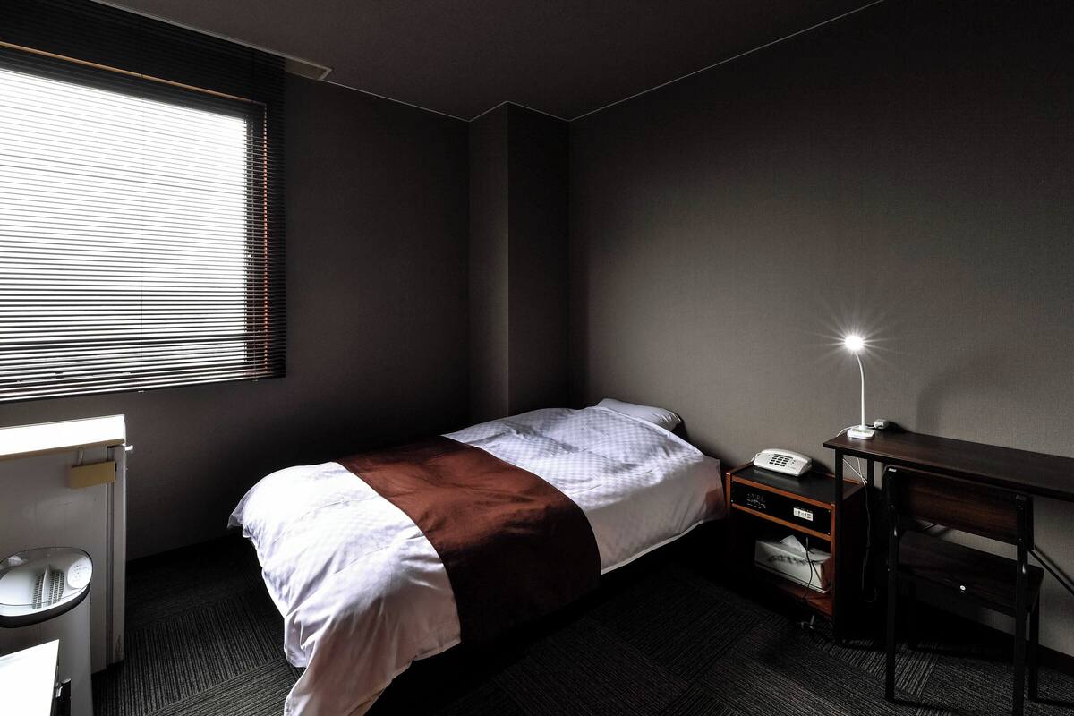 A small, modern hotel room with a single bed, a desk, and a chair.