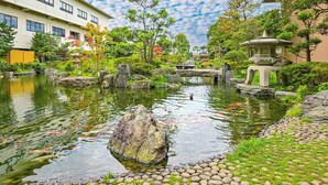 A serene garden with a pond, koi fish, and traditional Japanese structures. - Hokuriku Fukui Awara Onsen Mimatsu (Awara)