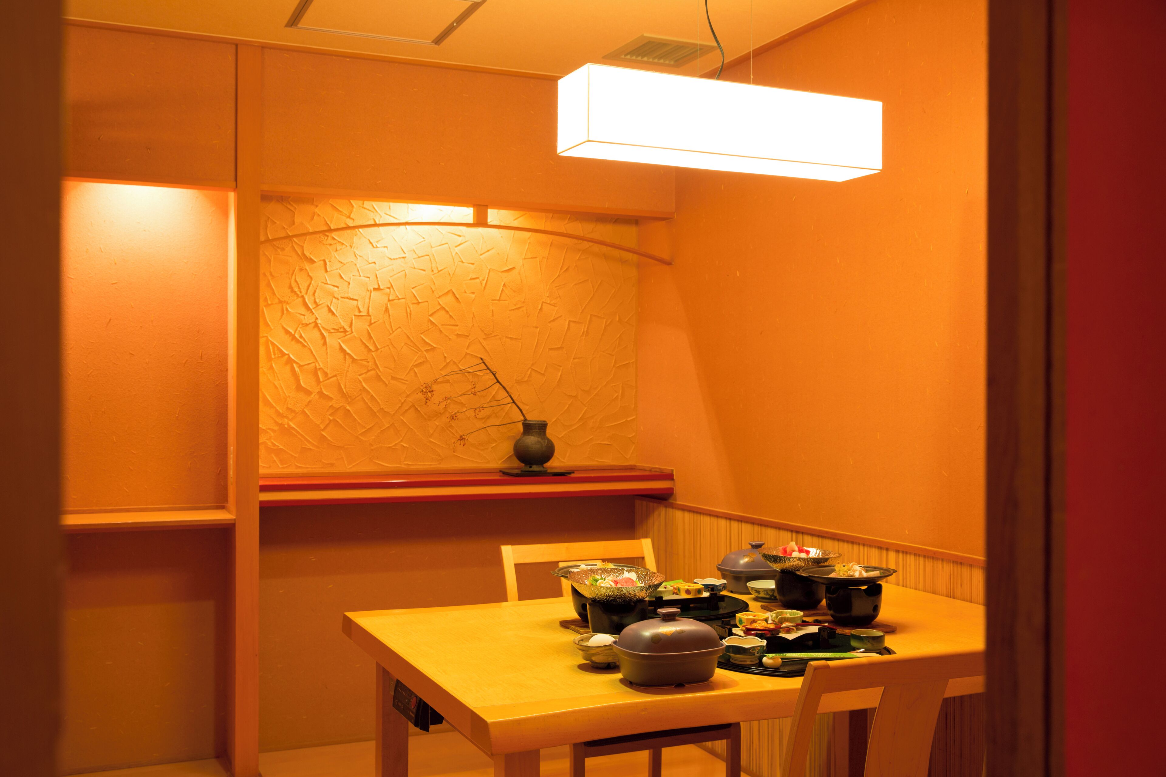 A dining area with a wooden table set for a meal, a vase on the wall, and a ceiling light fixture.