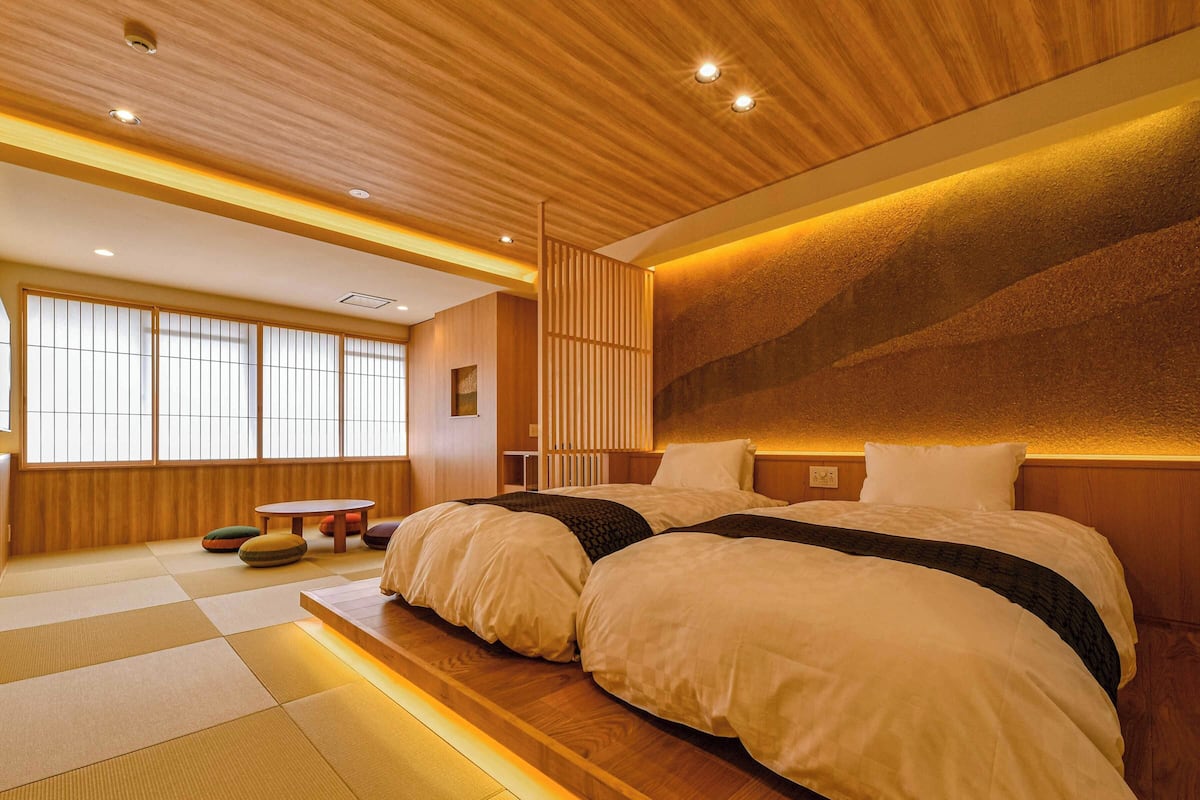 A spacious bedroom with a large bed, wooden flooring, tatami mats, a wooden headboard, and a sliding shoji screen.