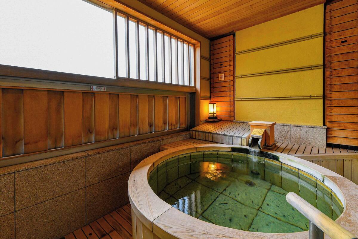 A traditional Japanese onsen with a wooden interior, a stone bath, and a wooden bench with a lantern.
