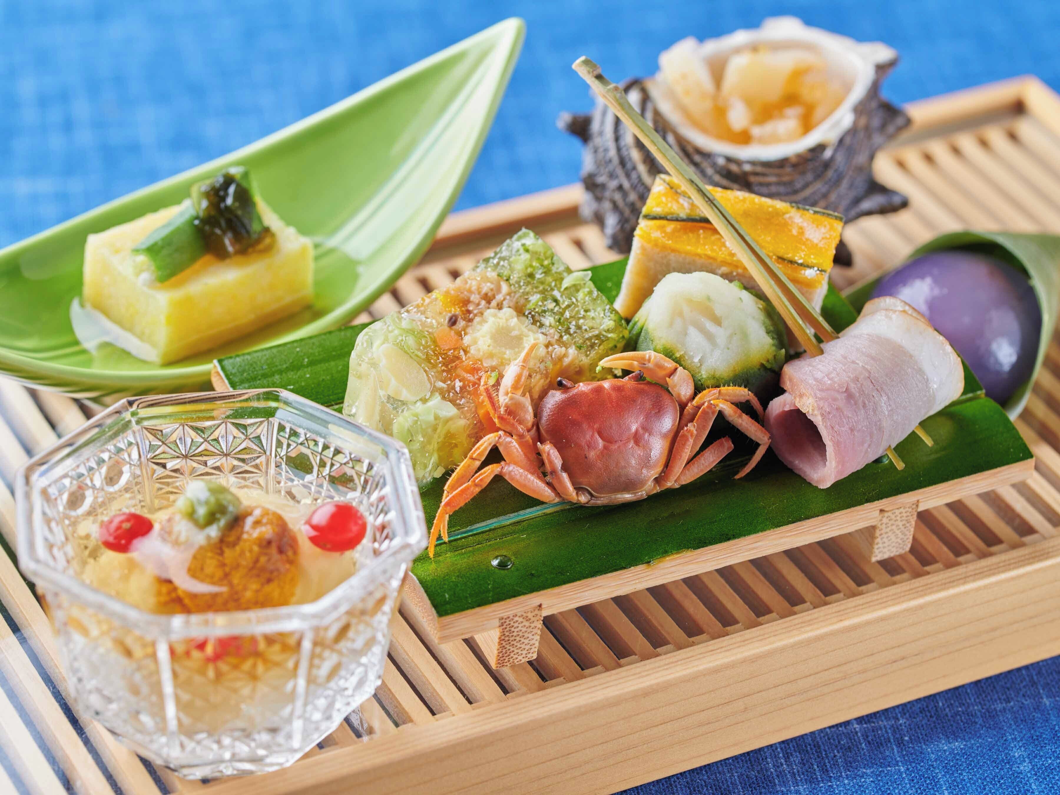A tray with various dishes including a crab, a yellow dessert, and a bowl with a red fruit.