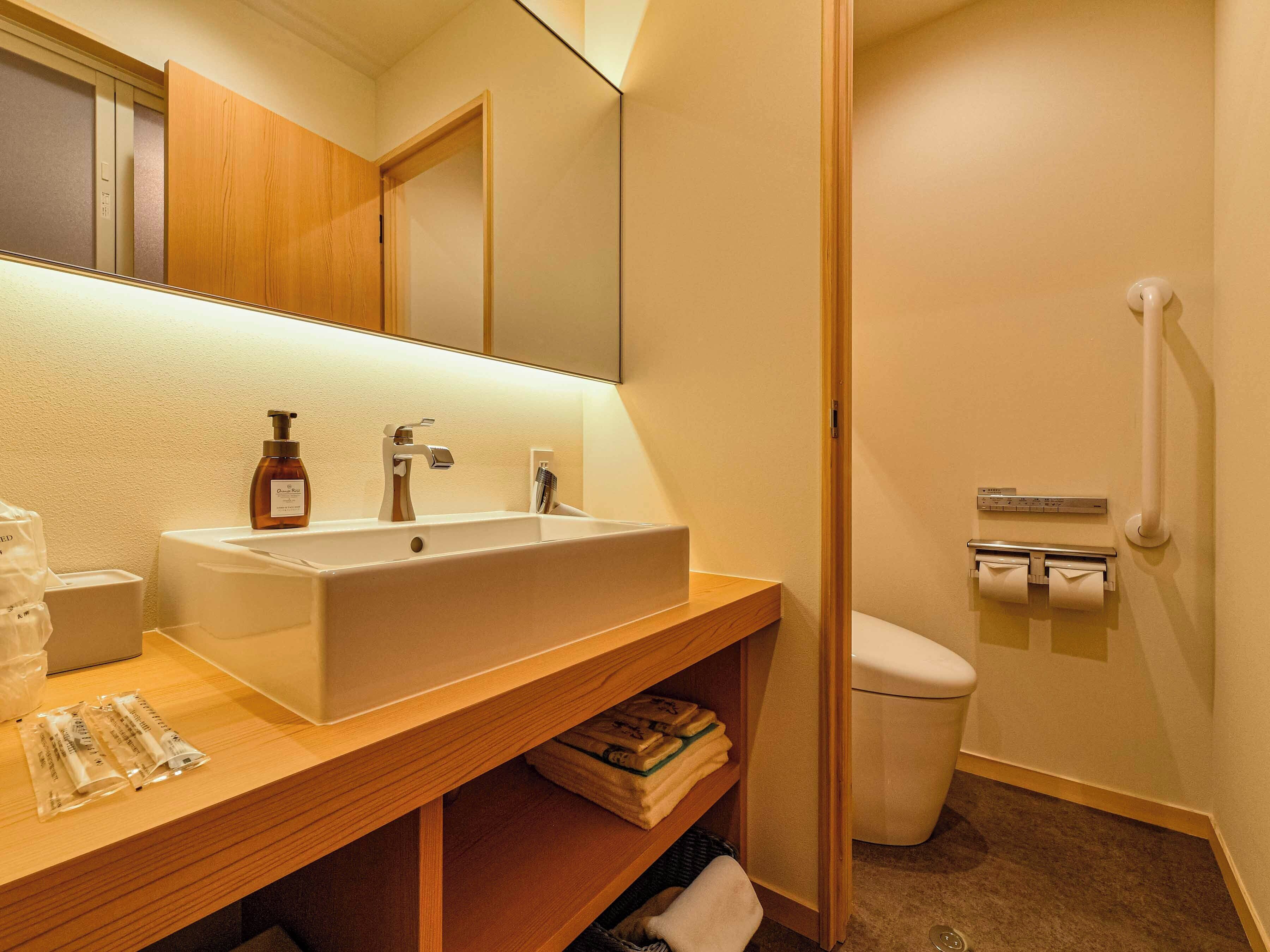 A bathroom with a wooden vanity, a white sink, a mirror, a toilet, and a hand dryer.