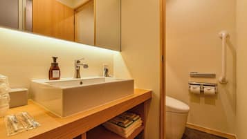 A bathroom with a wooden vanity, a white sink, a mirror, a toilet, and a hand dryer.