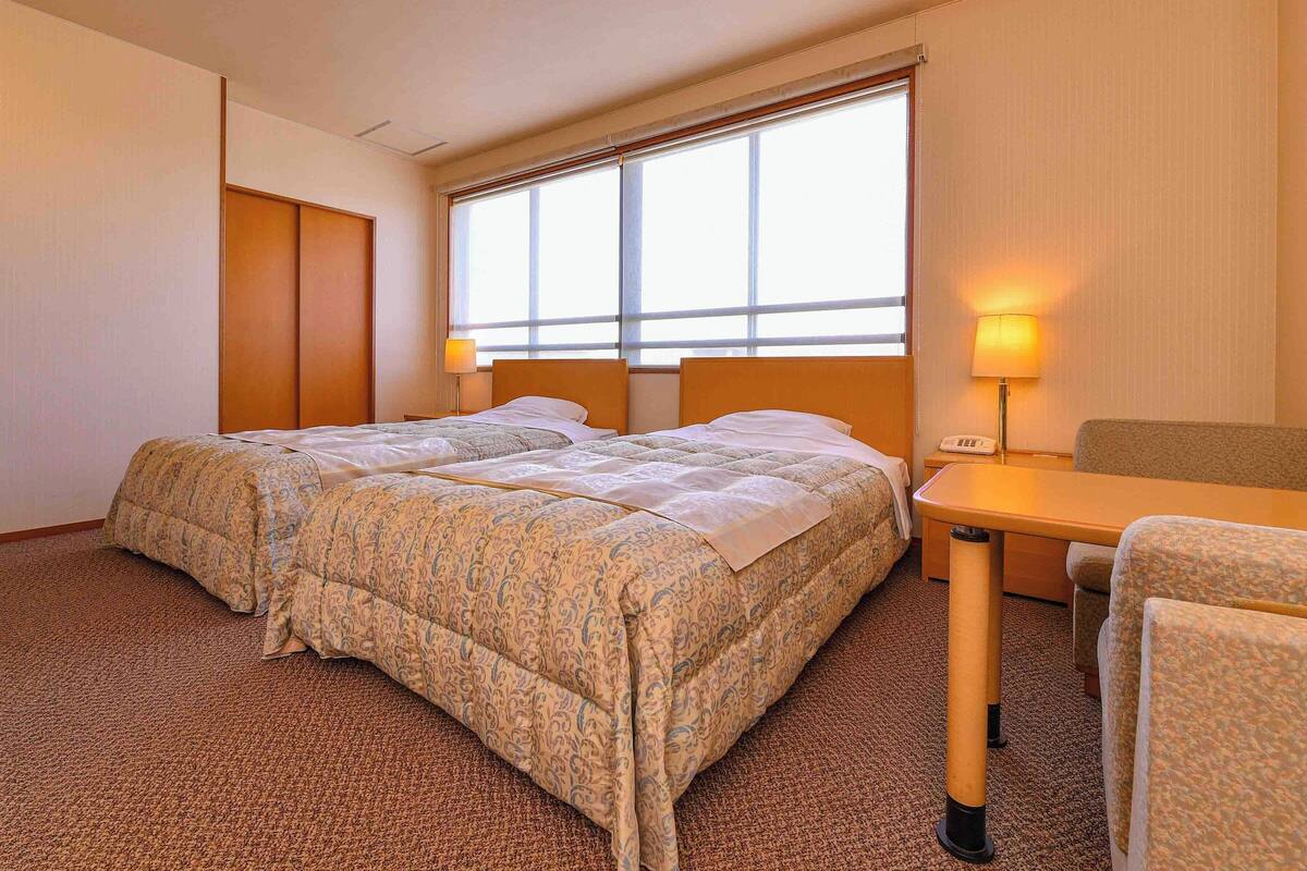 A hotel room with two beds, a desk, a chair, and a large window.