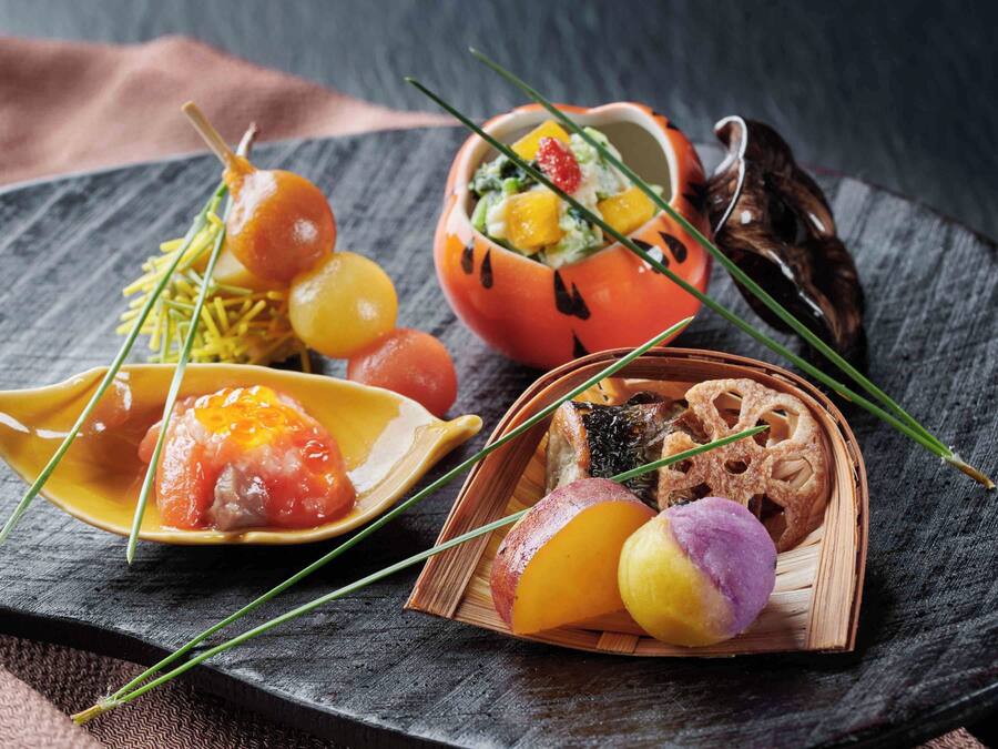 A variety of food items on a slate board, including a dish with grapes, a bowl with a fruit salad, and a plate with a piece of meat.