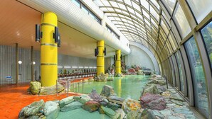 A spacious indoor swimming pool with a modern architectural design, featuring large yellow pillars and a glass ceiling. - Hokuriku Fukui Awara Onsen Mimatsu (Awara)