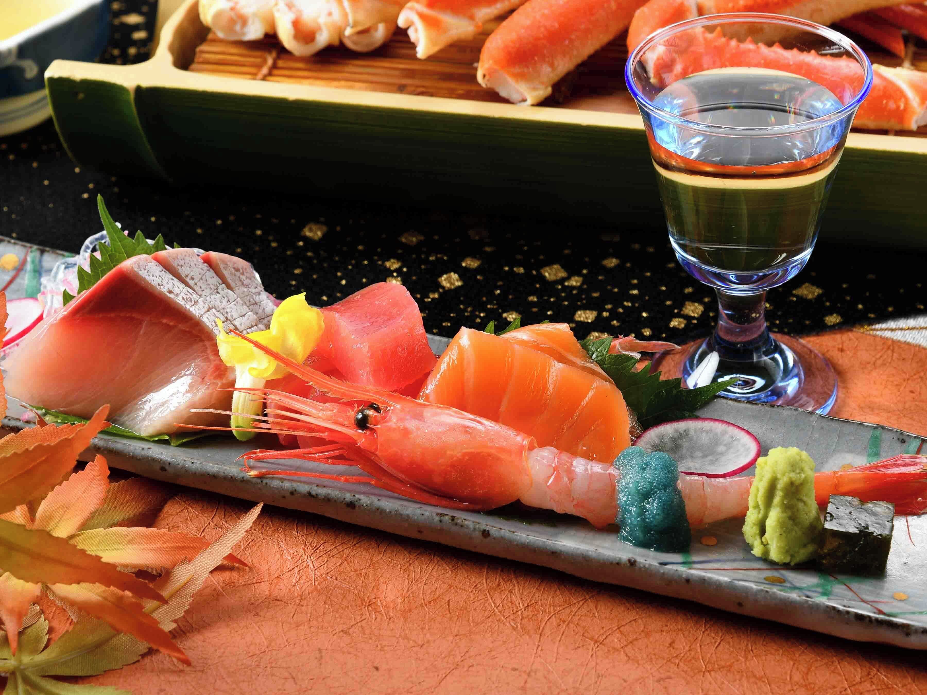 Eine Auswahl an Sushi auf einem Teller, darunter Garnelen, Fisch und Gemüse, mit einem Glas Sake daneben.
