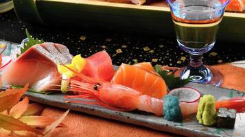 Eine Auswahl an Sushi auf einem Teller, darunter Garnelen, Fisch und Gemüse, mit einem Glas Sake daneben.