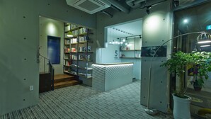 A modern reception area with a counter, bookshelves, and a staircase leading to another level. - Hotel The May (Gwangju)