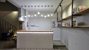 A reception area with a reception desk, multiple hanging lights, a staircase, and bookshelves with books. - Hotel The May (Gwangju)