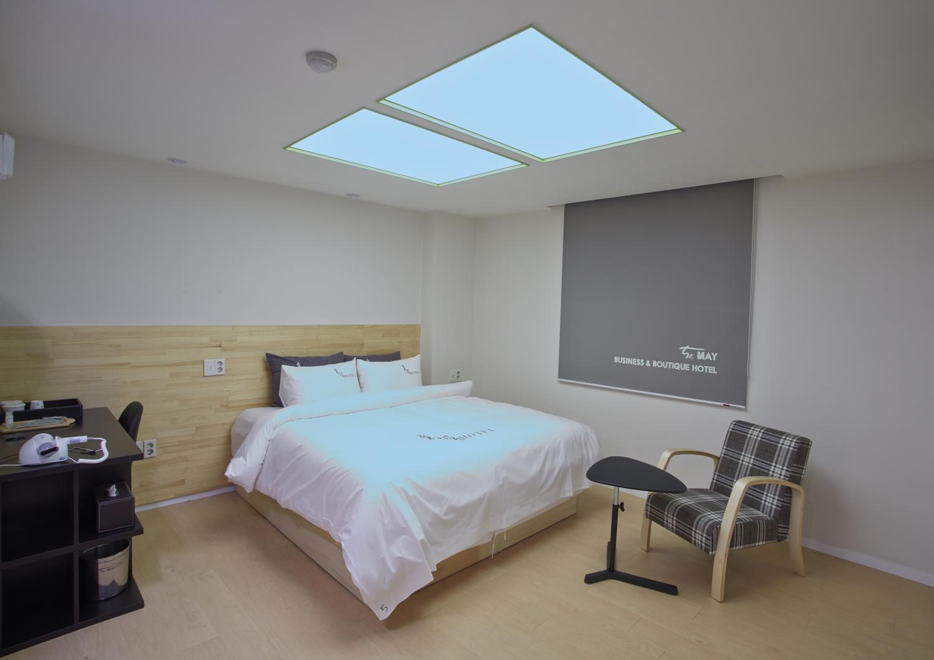 A hotel room with a bed, a desk, a chair, and a large window with skylights.