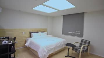 A hotel room with a bed, a desk, a chair, and a large window with skylights.