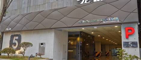 The exterior of a hotel with a modern design, featuring a prominent '5' sign, a glass entrance, and a 'P' parking sign.