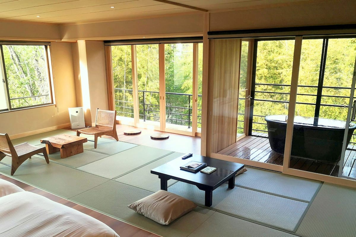 Una habitación tradicional japonesa con suelo de tatami, una mesa baja, una silla y un sofá.