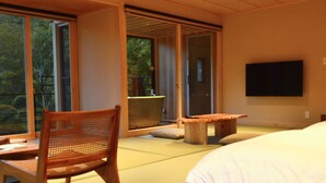 A room with tatami flooring, a wooden chair, a low table, a bed, and a TV mounted on the wall. - Tatsuta Ryokan (Izu)
