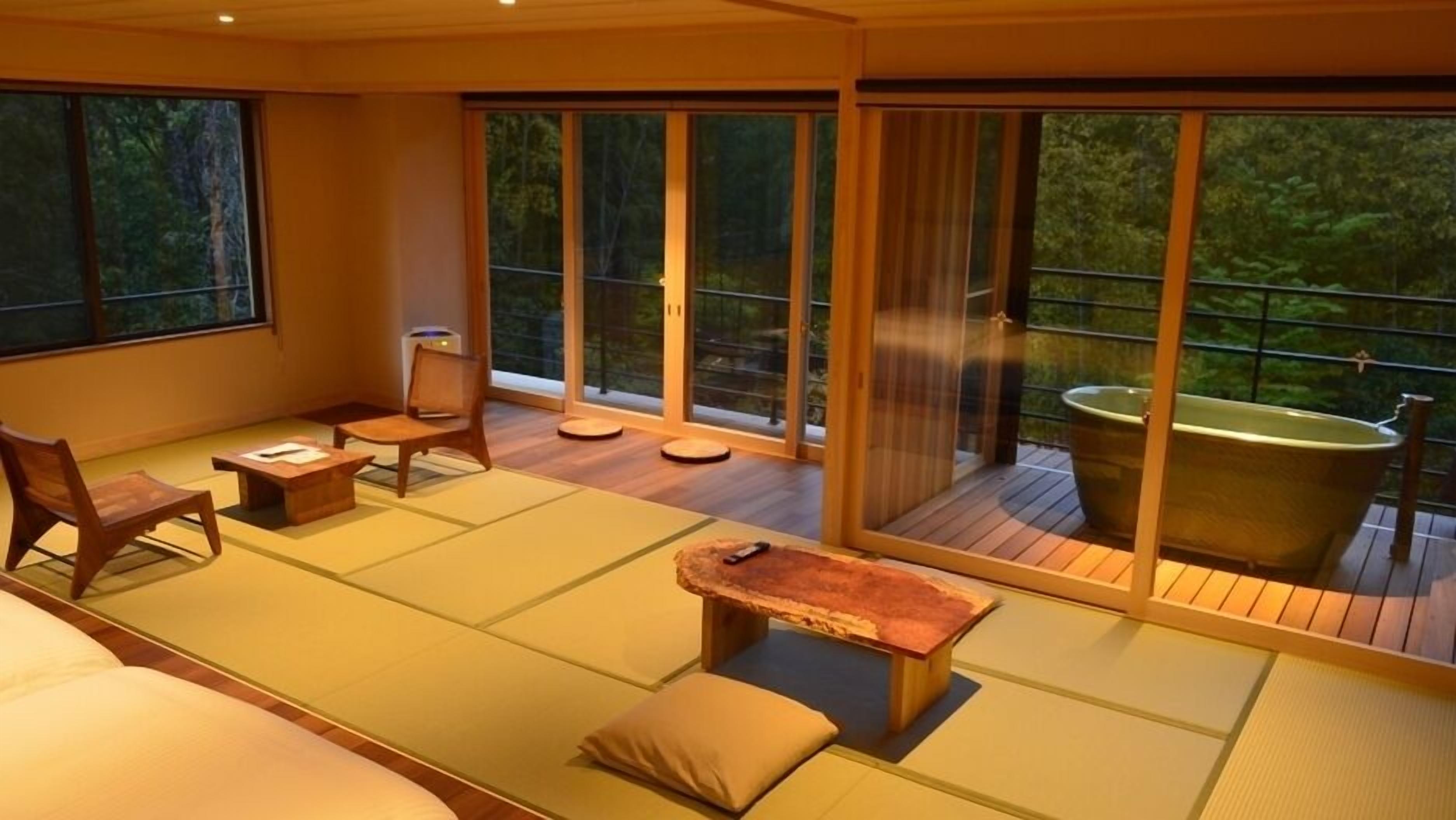 A room with tatami mats, a wooden table, chairs, a bathtub, and large sliding glass doors.