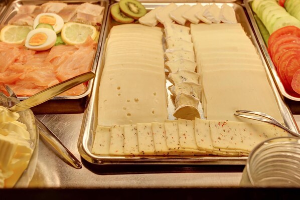 Un bufé con diversos alimentos, incluyendo salmón, queso y frutas cortadas.